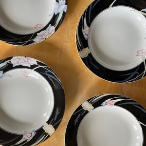 May include: Four white ceramic bowls with a black rim and floral design. The bowls have a gold trim and a pattern of irises in shades of pink, blue, and cream.