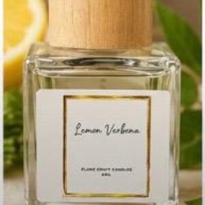 May include: A clear glass bottle with a light wood cap, containing a liquid. The white label features a gold border and the text Lemon Verbena, FLAME CRAFT CANDLES, 5ML. The bottle has a square base and a cylindrical neck with a wooden stopper.