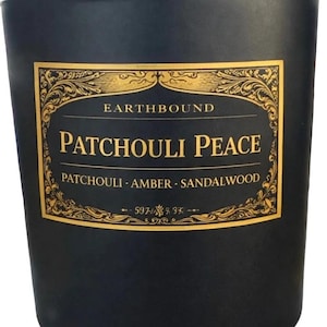 Puede incluir: Una vela negra con tapa de madera. La etiqueta dice "Earthbound Patchouli Peace" con notas de pachulí, ámbar y sándalo. La etiqueta es dorada con detalles ornamentados.