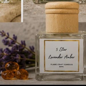 May include: A square glass bottle with a light wood cap, featuring a white label with a gold border. The label reads 5 Star Lavender Amber, Flame Craft Candles, 50ml. The bottle is accompanied by purple lavender sprigs and three amber-colored stones.