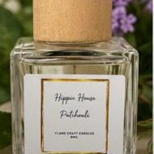 May include: A square glass bottle with a light wood cap containing liquid. The white label features a gold border and black text reading Hippie House Patchouli, FLAME CRAFT CANDLES, and 8ML. The bottle has a clear, transparent design.