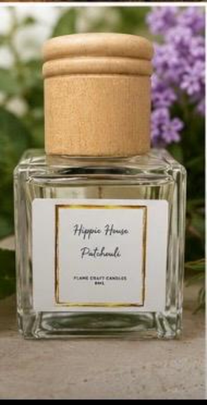 May include: A square glass bottle with a light wood cap containing liquid. The white label features a gold border and black text reading Hippie House Patchouli, FLAME CRAFT CANDLES, and 8ML. The bottle has a clear, transparent design.