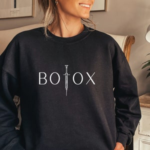 May include: Black sweatshirt with a white graphic of a syringe and the word "BOTOX" printed on the front.