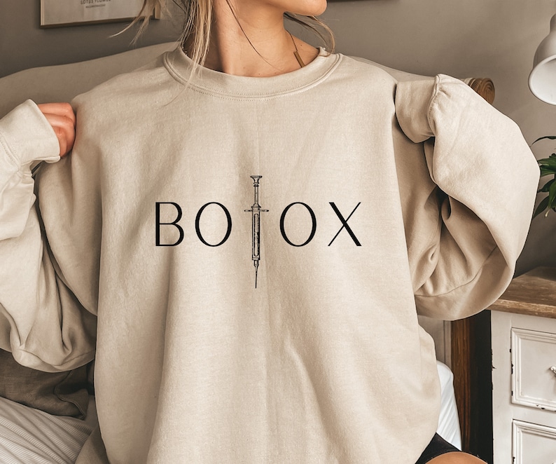 May include: A beige sweatshirt with the word "BOTOX" printed in black with a stylized syringe graphic.