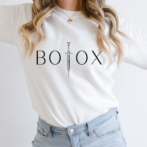 May include: White sweatshirt with the word "BOTOX" printed in black with a black and white illustration of a syringe in between the "O" and the "X".