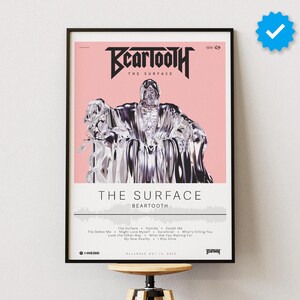 Puede incluir: Un póster enmarcado con fondo rosa que presenta una figura abstracta plateada. El título "Beartooth" se muestra en texto negro sobre la figura, y el título del álbum "The Surface" se muestra en texto negro debajo de la figura. La lista de canciones del álbum se muestra debajo del título del álbum.
