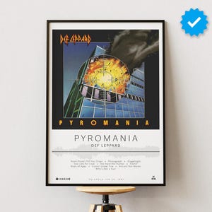 Könnte beinhalten: Gerahmtes Poster mit dem Albumcover von Def Leppards "Pyromania". Das Kunstwerk zeigt ein Gebäude mit einer feurigen Explosion in der Mitte. Der Bandname und der Albumtitel sind fett dargestellt.