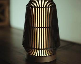 Può includere: Una lampada in bambù nero con un paralume marrone chiaro. La lampada è accesa e la luce brilla attraverso le lamelle di bambù.