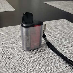 May include: A clear plastic case with a black and red vape device inside. The case has a black lanyard attached to it. The text "Breeze" is visible on the case.