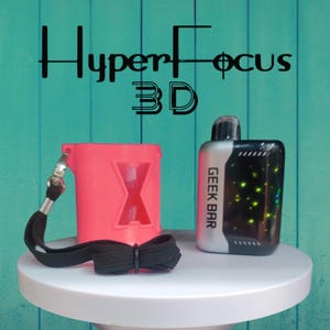 Op de afbeelding: Een roze 3D-geprinte hoes met een zwart koord en een zwarte strik, naast een Geek Bar vape. De hoes heeft een grote X-uitsparing. De vape is zwart en zilver met de woorden "GEEK BAR" aan de zijkant. De achtergrond heeft de woorden "HyperFocus 3D".