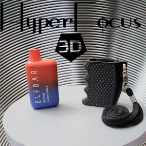May include: A red and blue disposable vape pen with the text "ELF BAR BC5000 SAKURA GRAPE" on the side. The vape pen is sitting on a white surface next to a black, textured, handheld device with a lanyard.