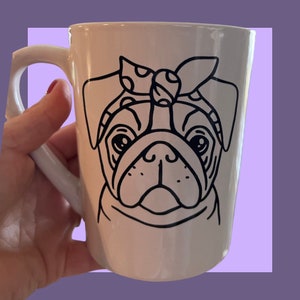 May include: White ceramic mug with a black line drawing of a pug wearing a polka dot bandana. The pug is looking directly at the viewer.