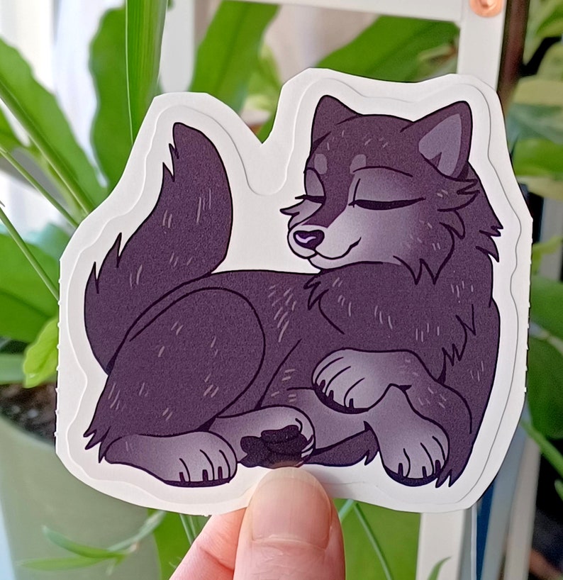 May include: A sticker featuring a cartoon wolf with a purple-grey color scheme. The wolf is lying down with its eyes closed, appearing to be sleeping. The sticker has a white background.