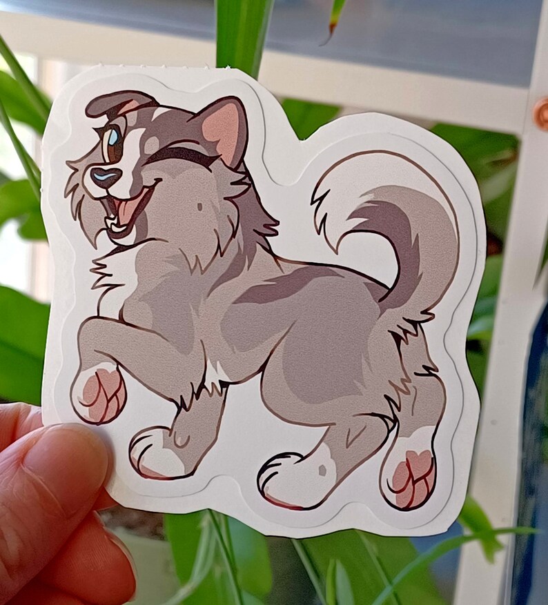 May include: A gray and white cartoon husky dog sticker with a happy expression, winking, and its tongue sticking out. The dog is standing on its hind legs with its front paws raised.