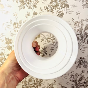 May include: White plastic ceiling light fixture with three concentric rings. The fixture has a large circular opening in the center.