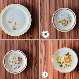 May include: Four vintage ceramic plates with floral designs. The plates feature various color schemes, including yellow, orange, and brown flowers on a white background. Each plate has a different floral pattern and a colored rim.