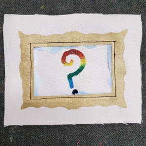 Puede incluir: Arte textil bordado con un marco dorado texturizado que rodea un lienzo blanco. Dentro del marco hay un signo de interrogación de color arcoíris. El fondo es una tela texturizada de color verde oscuro.