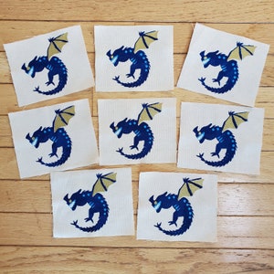 Peut inclure: Dix patchs thermocollants représentant un dragon bleu et or avec un sourire narquois. Le dragon a une aile jaune et un corps bleu avec des accents blancs.