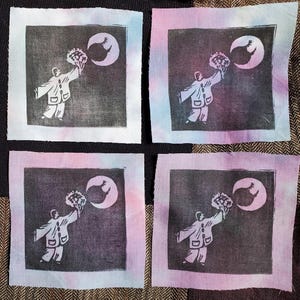May include: Four square fabric patches with a black and white print of a person holding a bouquet of flowers and reaching towards a crescent moon. The fabric patches have a pink and blue tie-dye background.