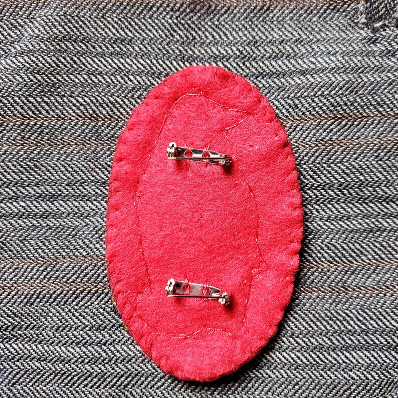 May include: The back of a red felt pin with two silver safety pins attached.