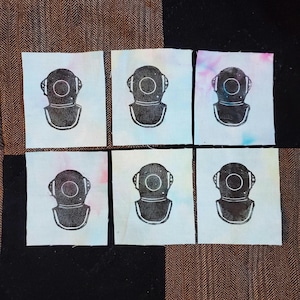 May include: Six white fabric squares with a black and white printed image of a diving helmet on each square.