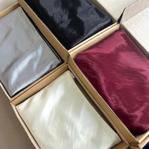 May include: An assortment of silk scarves in cardboard boxes. The scarves are in various colors, including black, silver, burgundy, and cream. The silk has a subtle sheen, and the boxes are arranged in a grid pattern.
