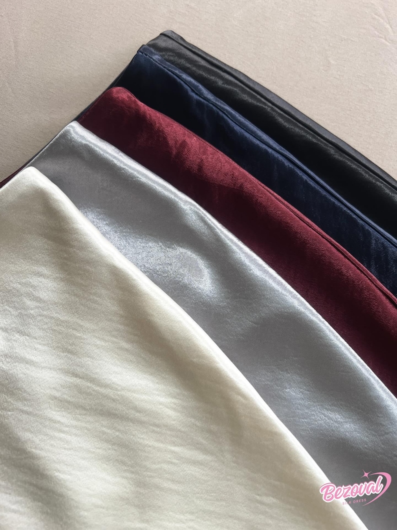 May include: An assortment of satin fabric in various colors, including ivory, silver, burgundy, navy, and black. The fabric is folded and arranged diagonally, showcasing the smooth texture and sheen of the material. The image is well-lit, highlighting the different shades.