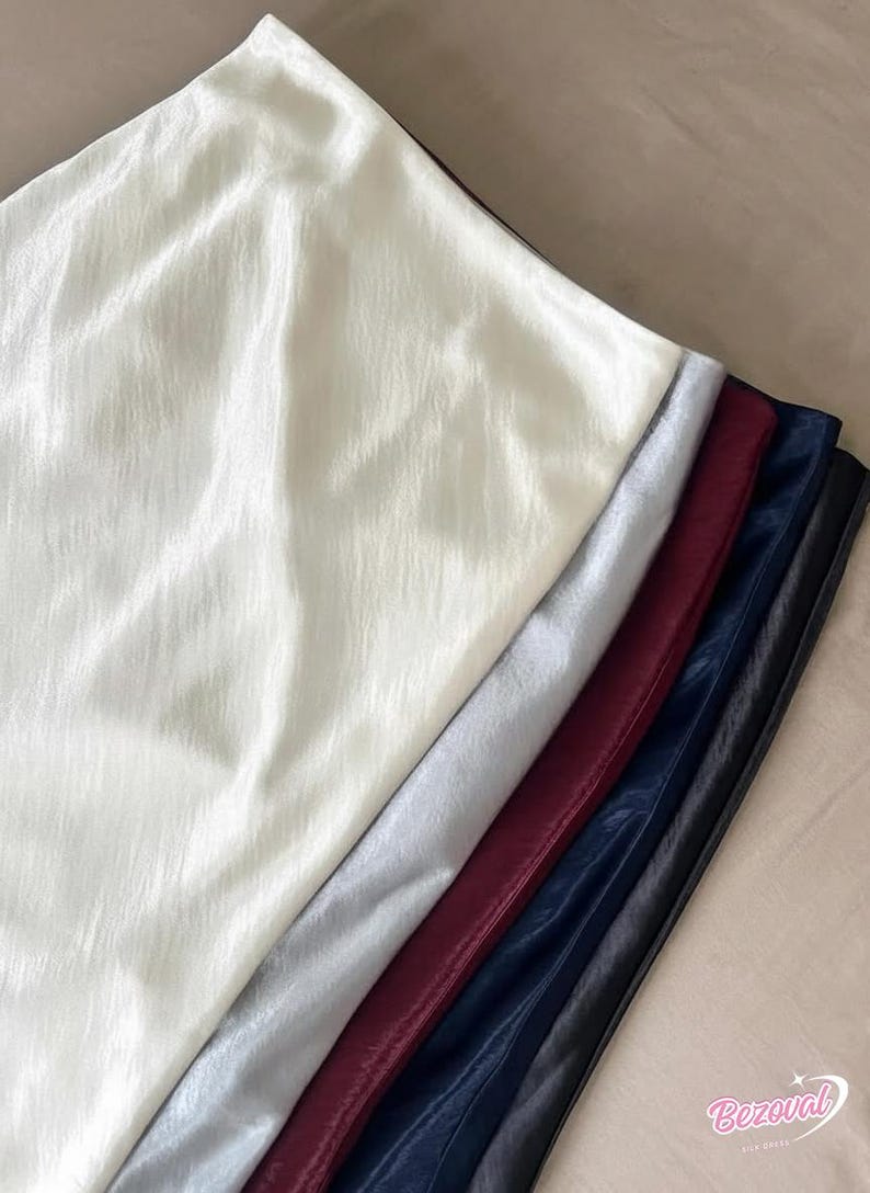 May include: A collection of fabric swatches in various colors, including off-white, silver, burgundy, navy blue, and black. The fabric has a shiny, slightly textured appearance, suggesting a satin or similar material. The swatches are arranged in a diagonal line.