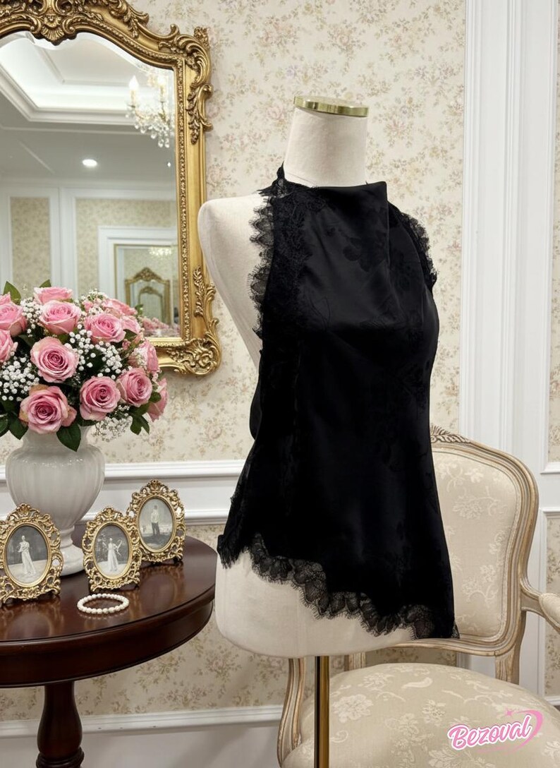 May include: A black halter top with lace trim, displayed on a mannequin. The top has a floral pattern and is set against a backdrop of a gold-framed mirror, pink roses, and antique decor.
