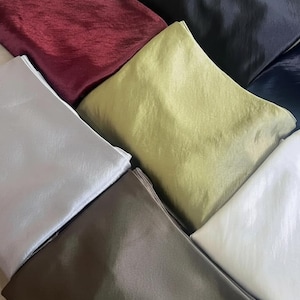 May include: An assortment of folded fabric squares in various colors, including burgundy, black, silver, olive green, brown, and white. The fabric has a shiny, textured appearance, suggesting a silk or satin material. The image is well-lit, showcasing the colors.