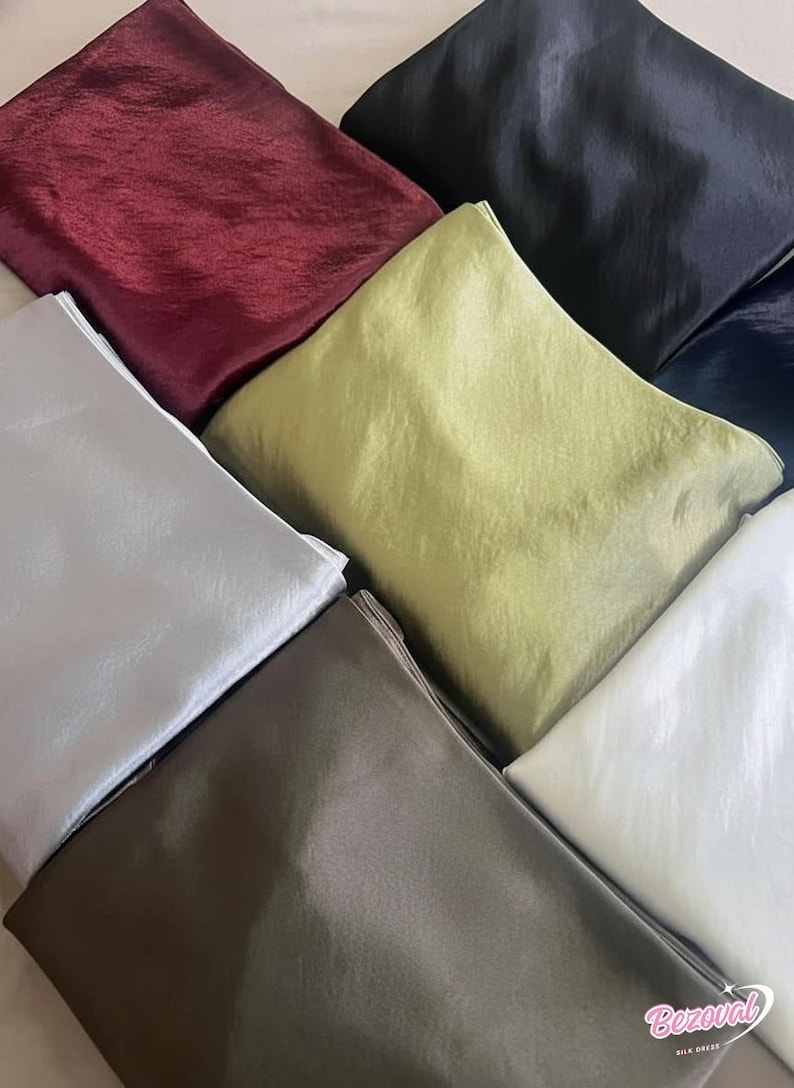 May include: An assortment of folded fabric squares in various colors, including burgundy, black, silver, olive green, brown, and white. The fabric has a shiny, textured appearance, suggesting a silk or satin material. The image is well-lit, showcasing the colors.