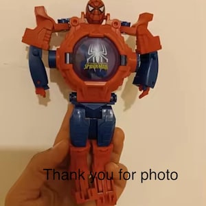 May include: Red and blue plastic toy robot with a Spider-Man face and the words "Amazing Spider-Man" on the chest. The robot has articulated arms and legs.