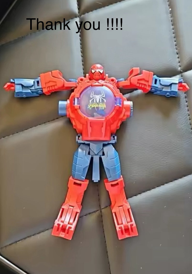 May include: A red and blue plastic toy robot with a Spider-Man design. The robot has a large head with a Spider-Man mask and a clear plastic window on the chest with the words "Spider-Man" printed on it.