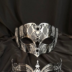 May include: A silver masquerade mask with a delicate, intricate design. The mask has a diamond pattern and a cutout around the eyes.