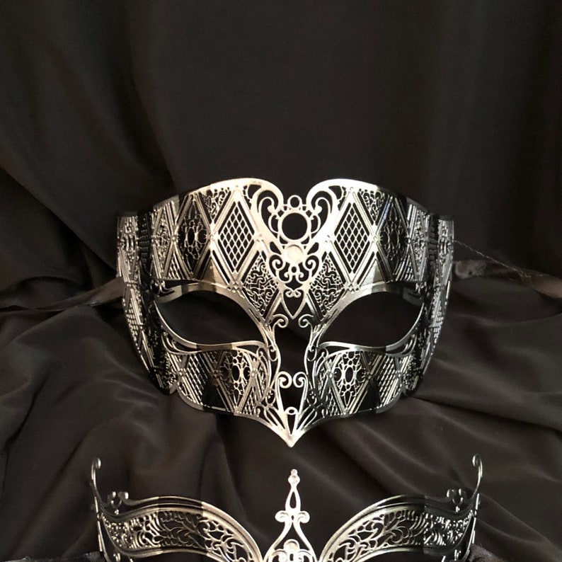May include: A silver masquerade mask with a delicate, intricate design. The mask has a diamond pattern and a cutout around the eyes.