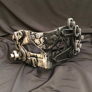 May include: A black and silver steampunk-style masquerade mask with intricate gears and a black lace eye covering.