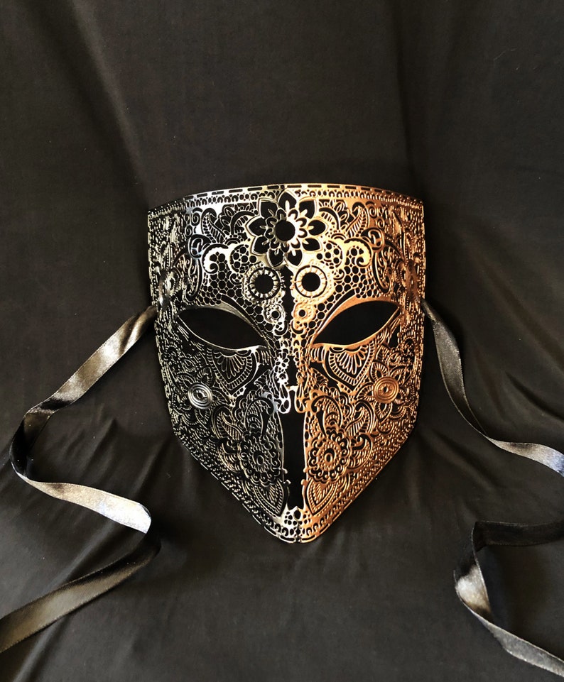 May include: A black and gold masquerade mask with intricate cut-out designs. The mask has two black ribbons attached to the sides.