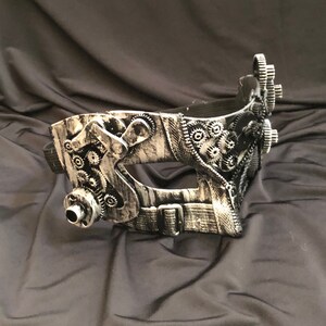 May include: A silver and black steampunk-style masquerade mask with intricate gear details and a black strap.