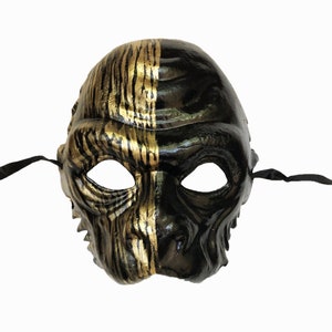 May include: A black and gold masquerade mask with a textured, sculpted design. One side of the mask is black, and the other side is gold with a zebra-like pattern.