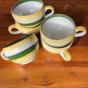 May include: A set of three ceramic mugs with a speckled, matte finish in cream, light grey, and dark grey. Each mug has a simple, minimalist design and a rounded handle.