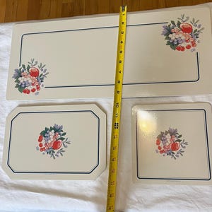 Peut inclure: Un ensemble de quatre sets de table et un chemin de table crème avec un motif de fruits. Le chemin de table mesure environ 40 cm de large et 61 cm de long. Chaque pièce a une bordure bleu foncé et un motif de grappe de fruits.
