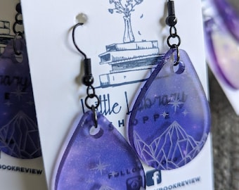 Könnte beinhalten: Lilafarbene tropfenförmige Harzohrringe mit einem weißen geometrischen Muster und silbernem Glitzer. Die Ohrringe befinden sich auf einer weißen Karte mit dem Text "Little Library Shoppe" und "Follow @thelittlebookshoppe" darauf.