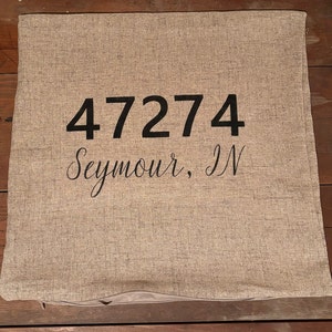 May include: A beige linen pillow with black embroidery that reads "47274 Seymour, IN".