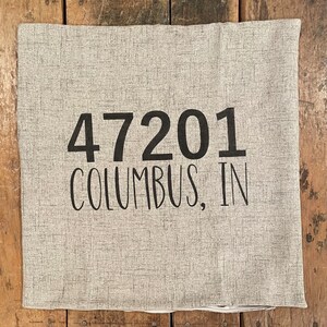 May include: A gray linen pillow with black text that reads "47201 Columbus, IN".