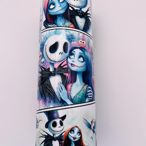 May include: A white tumbler with a colorful design featuring Jack Skellington and Sally from the Nightmare Before Christmas. The design is in a comic book style with multiple panels showing the couple in different poses.