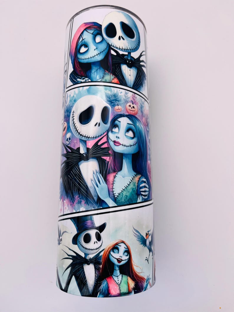 May include: A white tumbler with a colorful design featuring Jack Skellington and Sally from the Nightmare Before Christmas. The design is in a comic book style with multiple panels showing the couple in different poses.