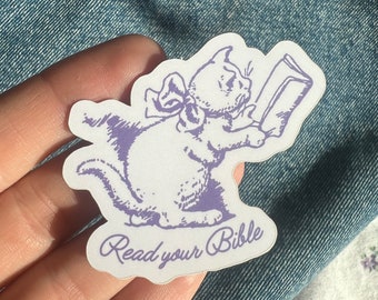 May include: A purple and white sticker with a cartoon cat reading a book. The text on the sticker says "Read your Bible".