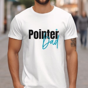 May include: White t-shirt with black text that says "Pointer Dad" with a small paw print symbol above the word "Dad". The word "Dad" is written in a blue cursive font.