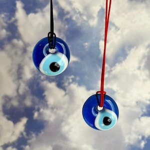 May include: Two evil eye necklaces with blue glass pendants on black and red cords. The pendants are round and have a white and blue eye design.