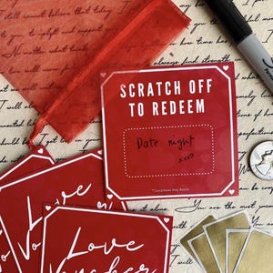 May include: A collection of red love vouchers and scratch-off cards with white text and borders. One card reads "Scratch Off To Redeem" with "Date night" written below. A red mesh gift bag and a black marker are also visible.